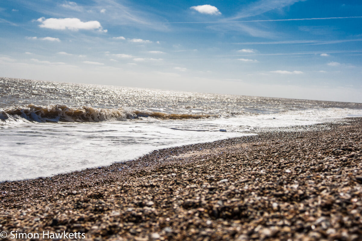 Dunwich Heath Suffolk pictures - Waves breaking over the pebbles against a blue sky